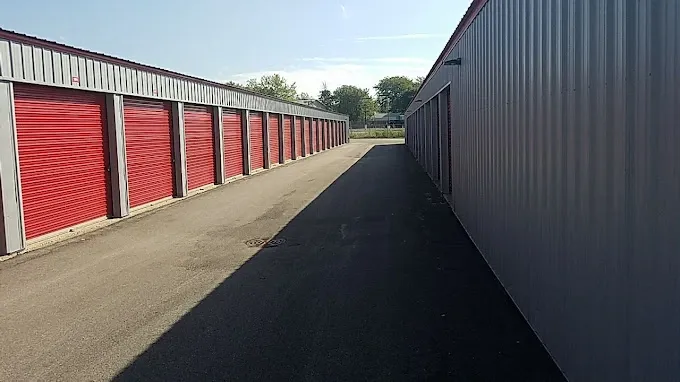 Outdoor storage units with red roll-up doors and paved vehicle access